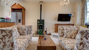 Una sala de estar con dos sofás estampados, una mesa de centro de madera, un televisor y una estufa verde.