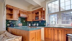 A kitchen with wooden cabinets, a green tiled backsplash, and a large window. - Carnegie Library Shakespeare Apartment 3 bed (Swinton)