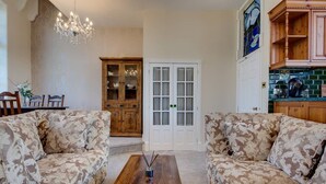 A living room with two patterned sofas, a wooden coffee table, a chandelier, a cabinet, and a door with glass panels. - Carnegie Library Shakespeare Apartment 3 bed (Swinton)