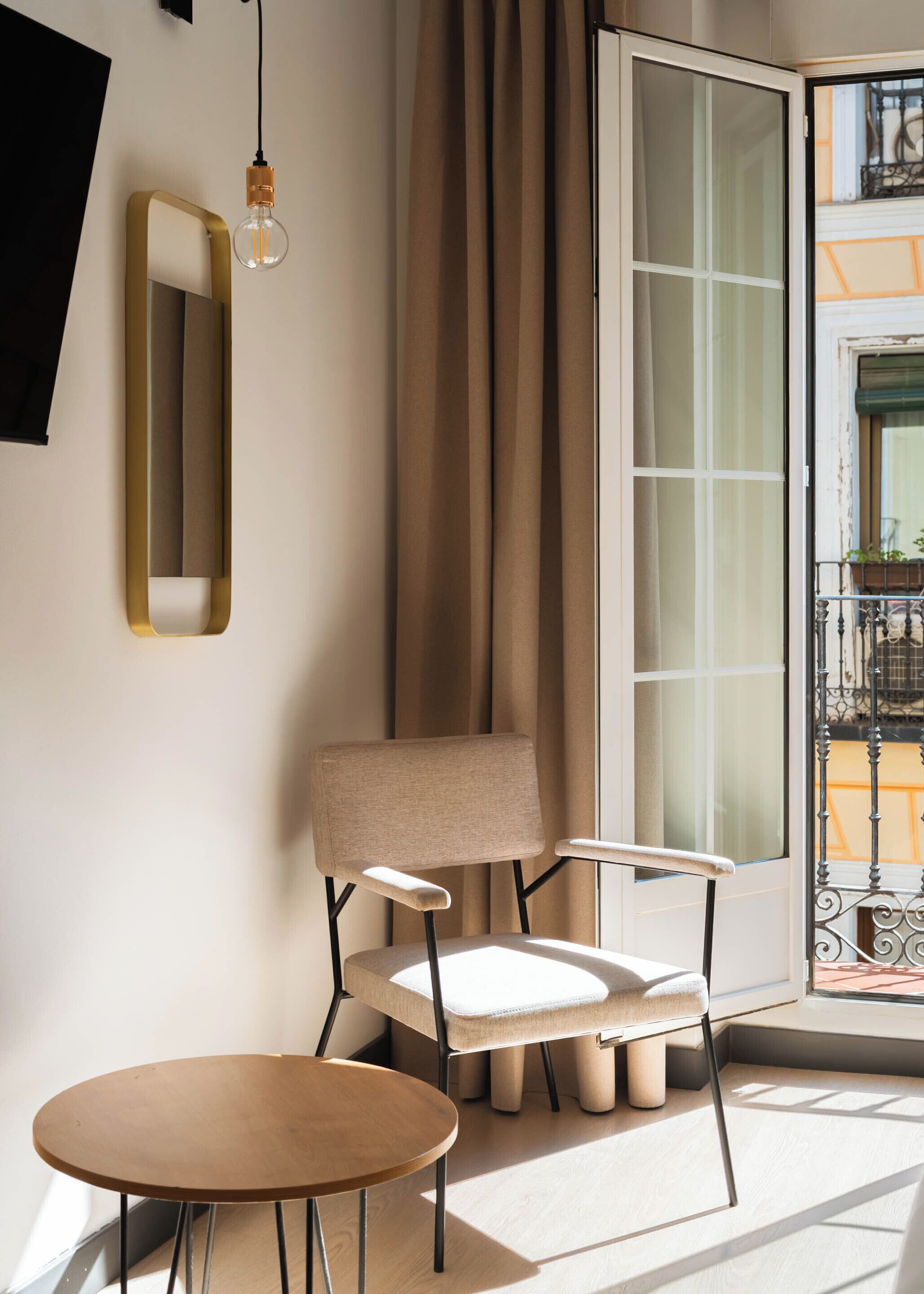 A modern room with a large window, a chair, a small table, and a hanging light fixture.