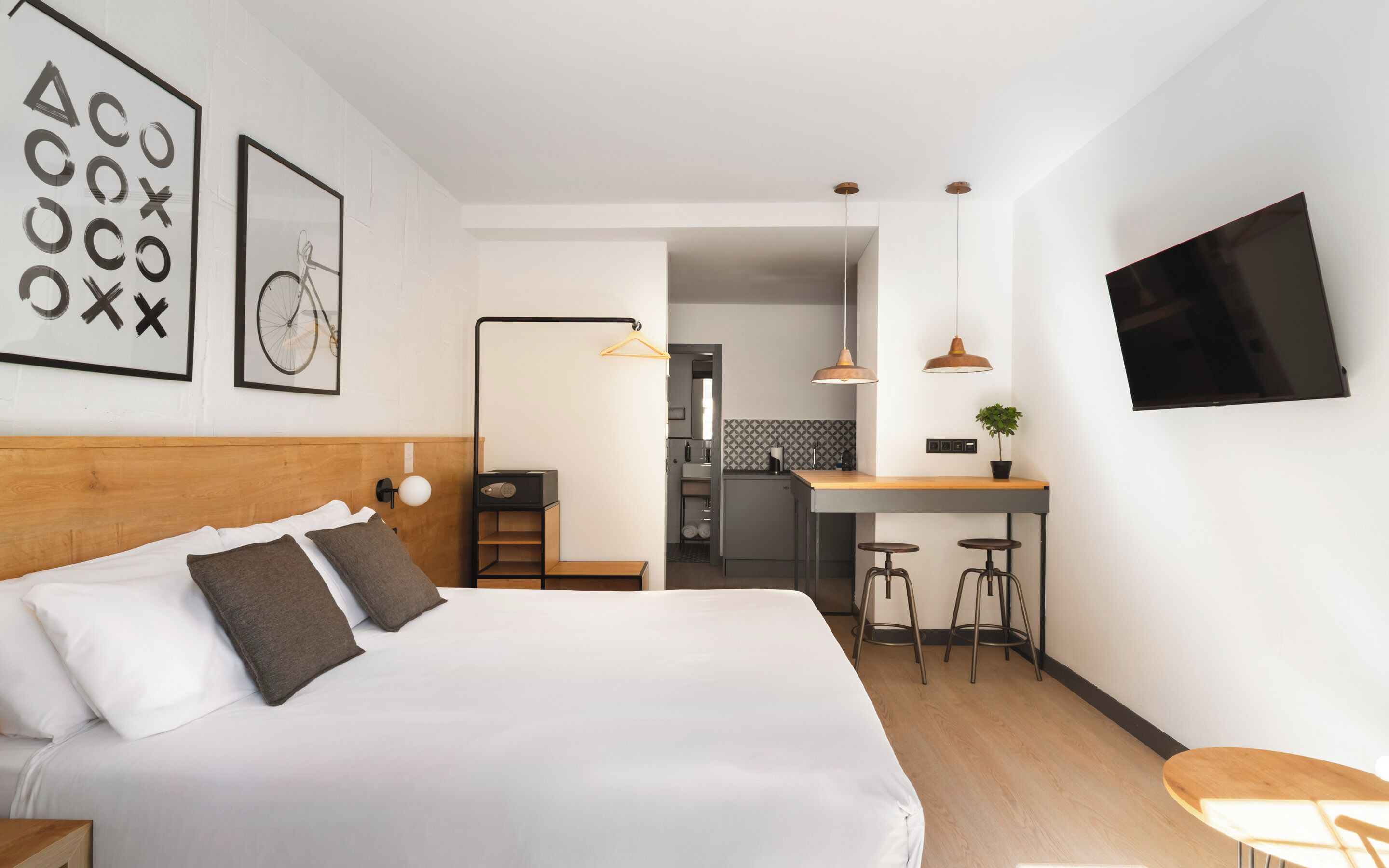 Ein modernes Hotelzimmer mit einem großen Bett, einem Schreibtisch mit Hocker, einem Fernseher und einer Küchenzeile.