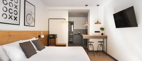 Ein modernes Hotelzimmer mit einem großen Bett, einem Schreibtisch mit Hocker, einem Fernseher und einer Küchenzeile.