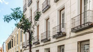 Un edificio de varios pisos con balcones, un coche aparcado y un árbol en la acera.