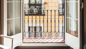 Un balcón con barandilla de metal, una ventana con vista a un edificio y una puerta que da al interior.