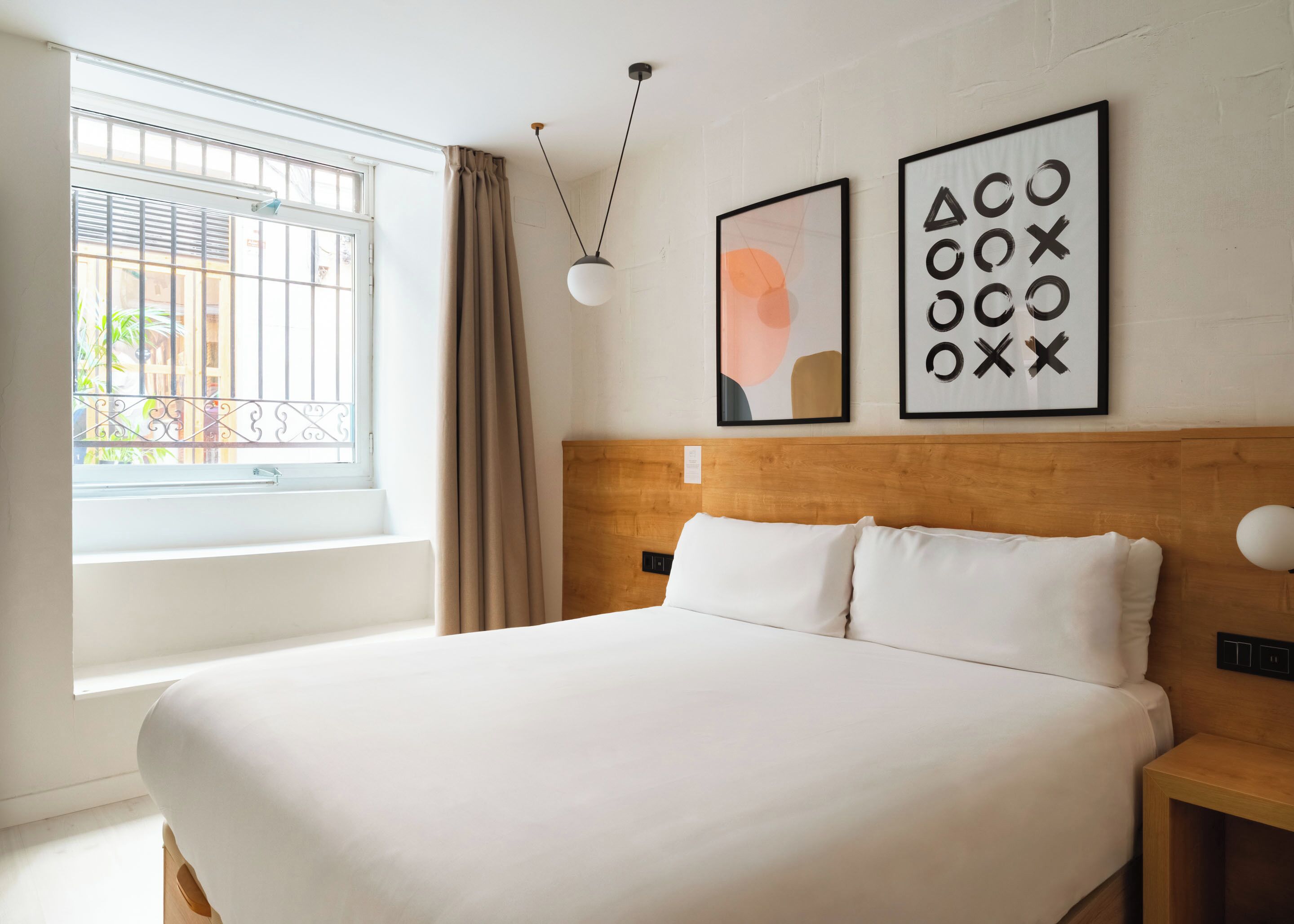 A hotel room with a large bed, a window with a view, and two framed pictures on the wall.