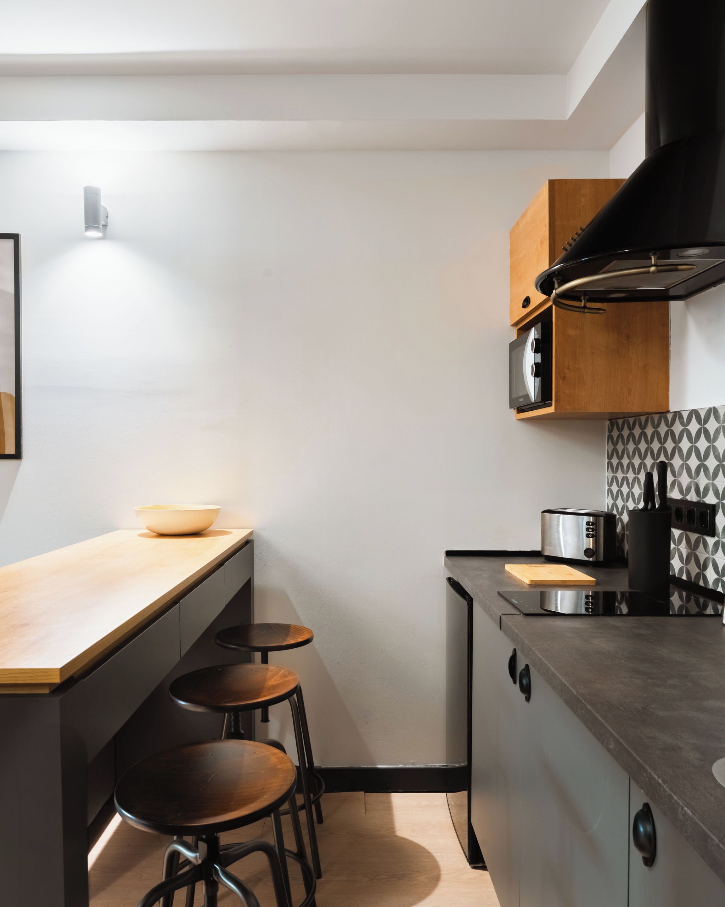 Una cocina moderna con encimera de madera, dos taburetes, un tostador y una campana extractora negra.