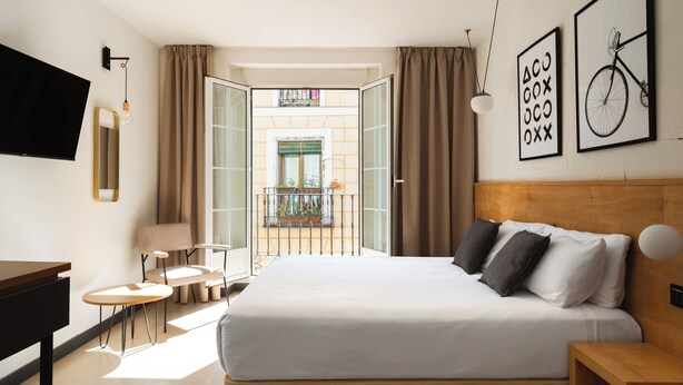 Habitación de hotel con cama, mesitas de noche, escritorio, televisión y balcón con plantas.