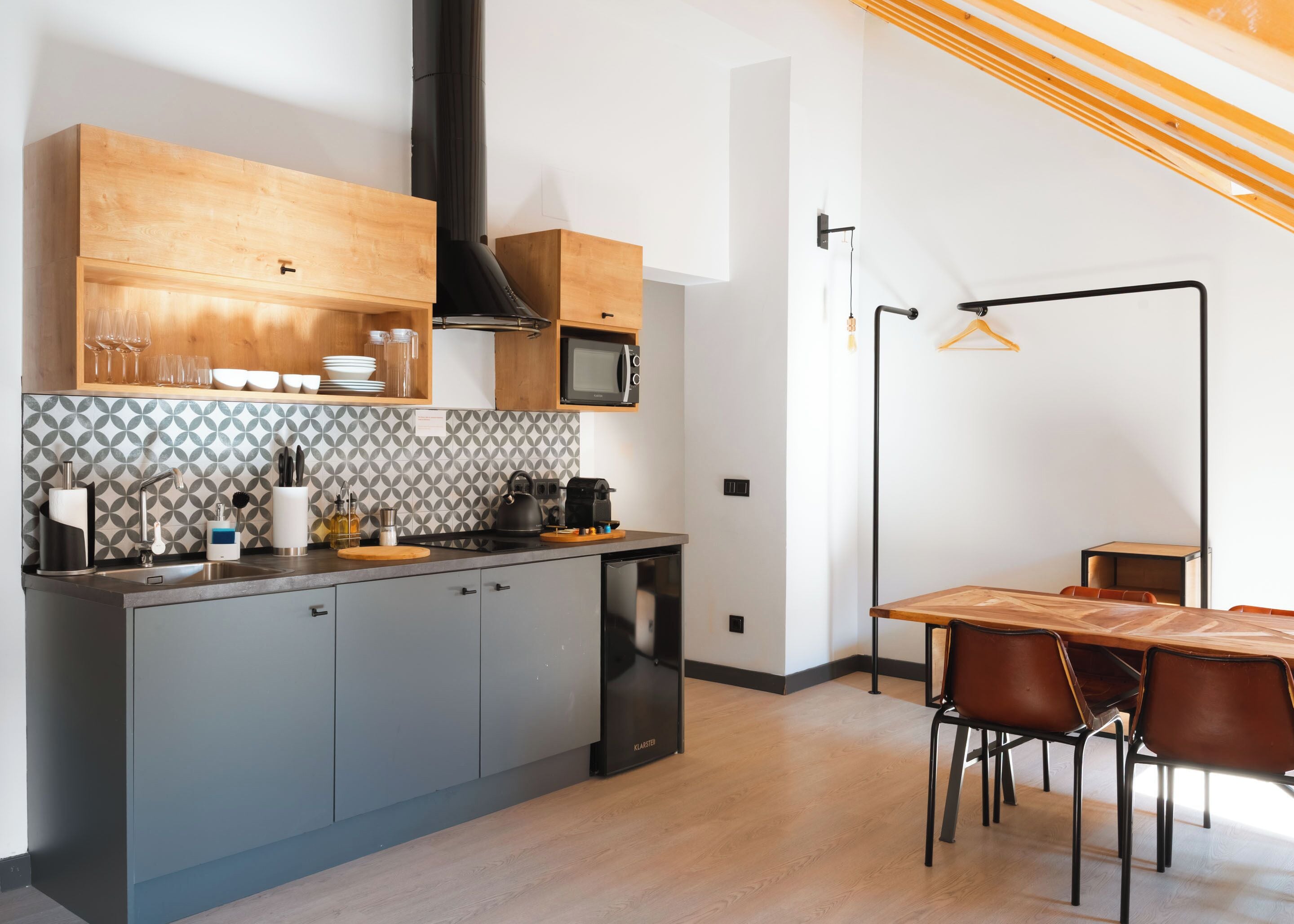 A modern kitchen with grey cabinets, a wooden countertop, a built-in microwave, and a kettle.