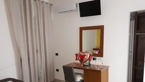 Una habitación con un escritorio de madera, una silla, un espejo, un televisor de pantalla plana y una cama.