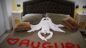 Una cama con una toalla blanca grande con forma de langostino y un corazón hecho de pétalos de rosa que deletrea "DAUGURI".