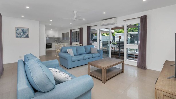 Ein modernes Wohnzimmer mit einem blauen Sofa, einem Holztisch und einer Küche im Hintergrund.