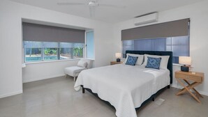 Ein modernes Schlafzimmer mit einem großen Bett, zwei Nachttischen, einem Deckenventilator und einem Fenster mit Blick auf einen Swimmingpool.