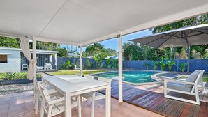 Eine überdachte Terrasse mit Pool, weißen Möbeln und einer Holzterrasse.
