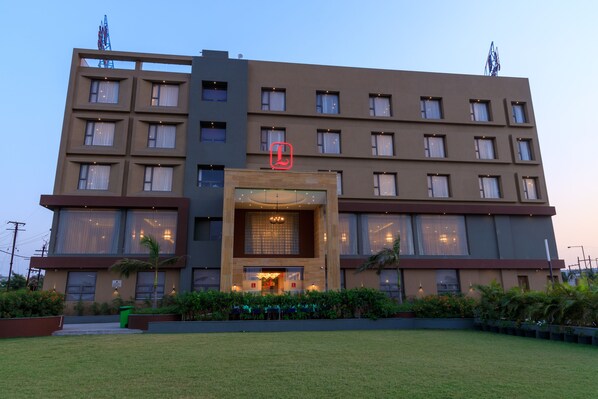 A multi-story hotel with a central entrance, large windows, and a well-maintained lawn. - Lords Eco Inn Jamnagar (Jamnagar)