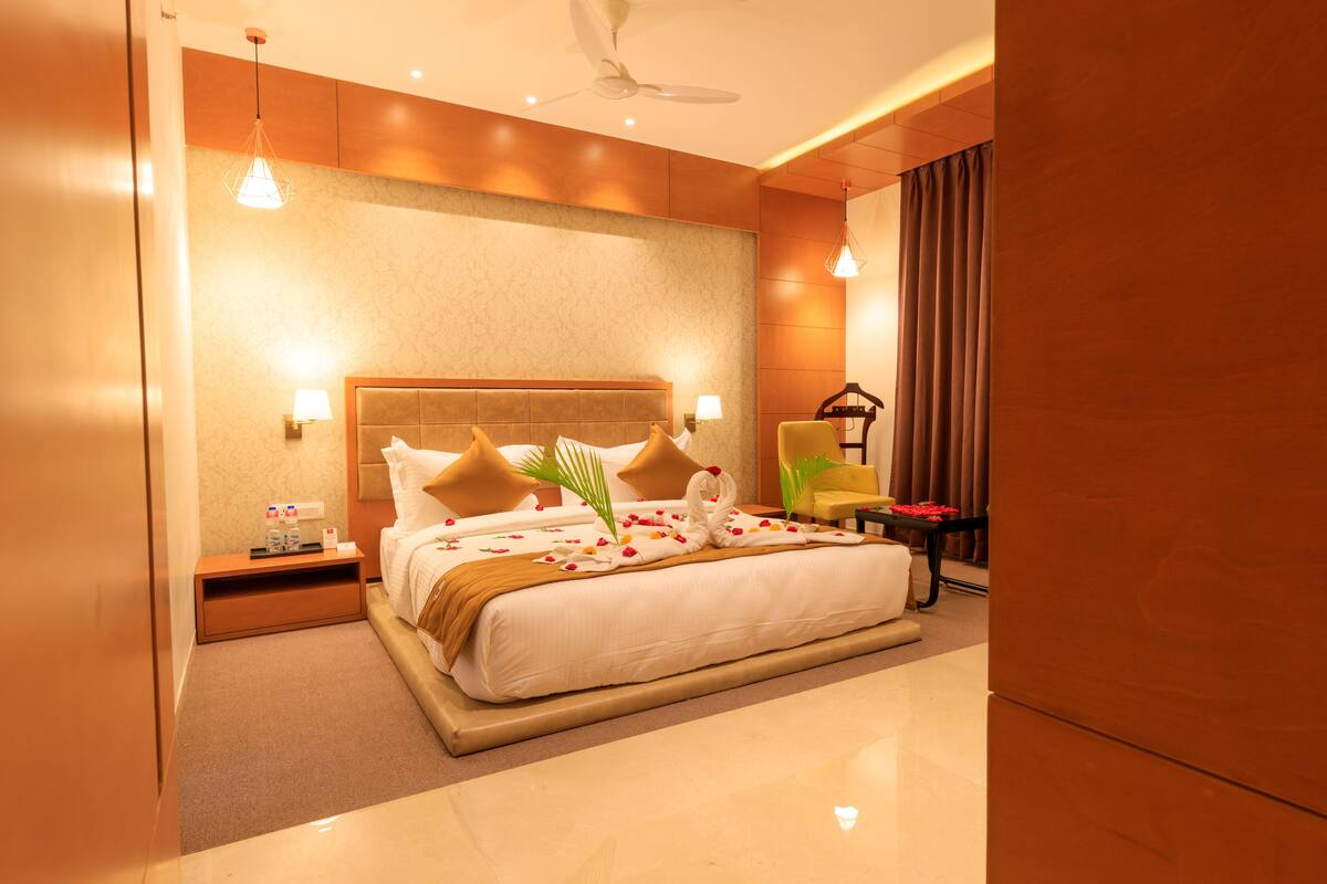 A modern hotel room with a large bed, a bedside table, a nightstand, a chair, a desk, and a ceiling fan.