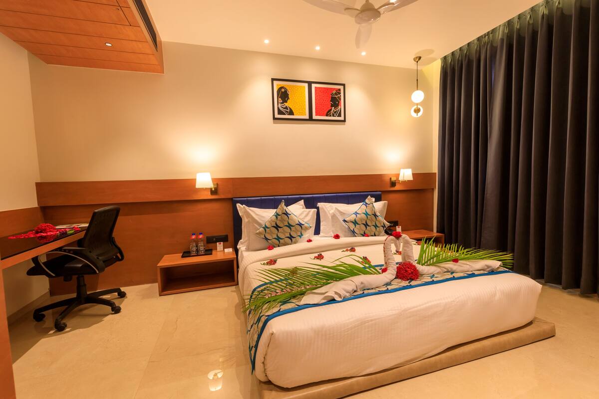 A hotel room with a large bed, a desk, a chair, and a nightstand.