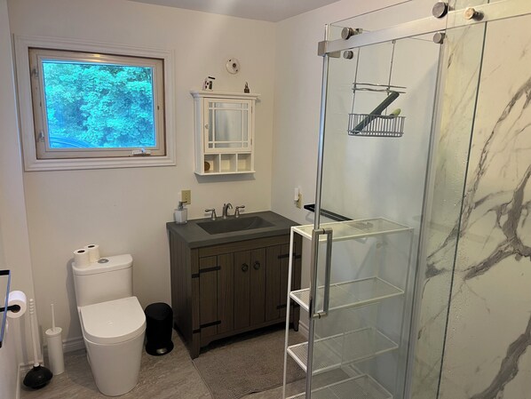 Un bagno con il water, lavandino, doccia e una finestra con vista sugli alberi.