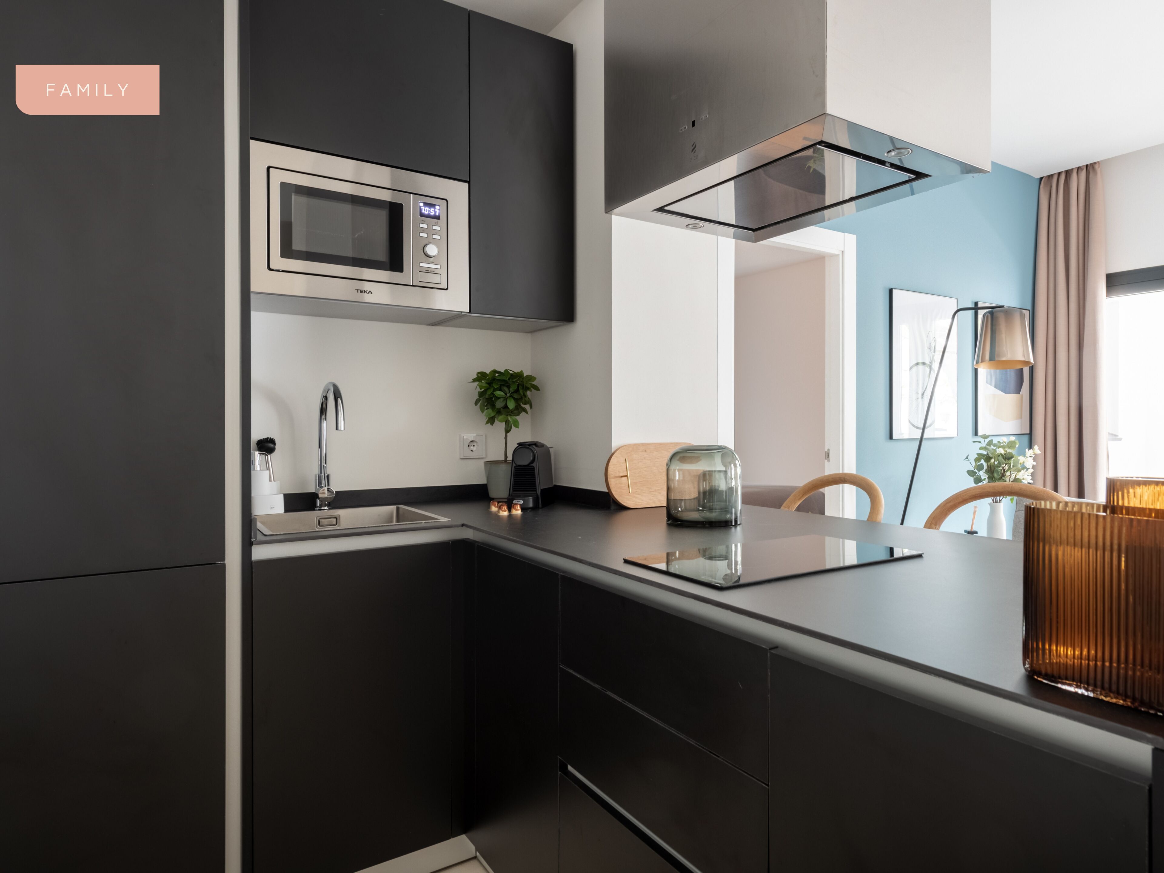Une cuisine moderne avec des meubles de couleur sombre, un four à micro-ondes en acier inoxydable et un four encastré. On y trouve une plante sur le plan de travail et un grille-pain.