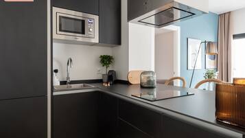 Une cuisine moderne avec des meubles de couleur sombre, un four à micro-ondes en acier inoxydable et un four encastré. On y trouve une plante sur le plan de travail et un grille-pain.