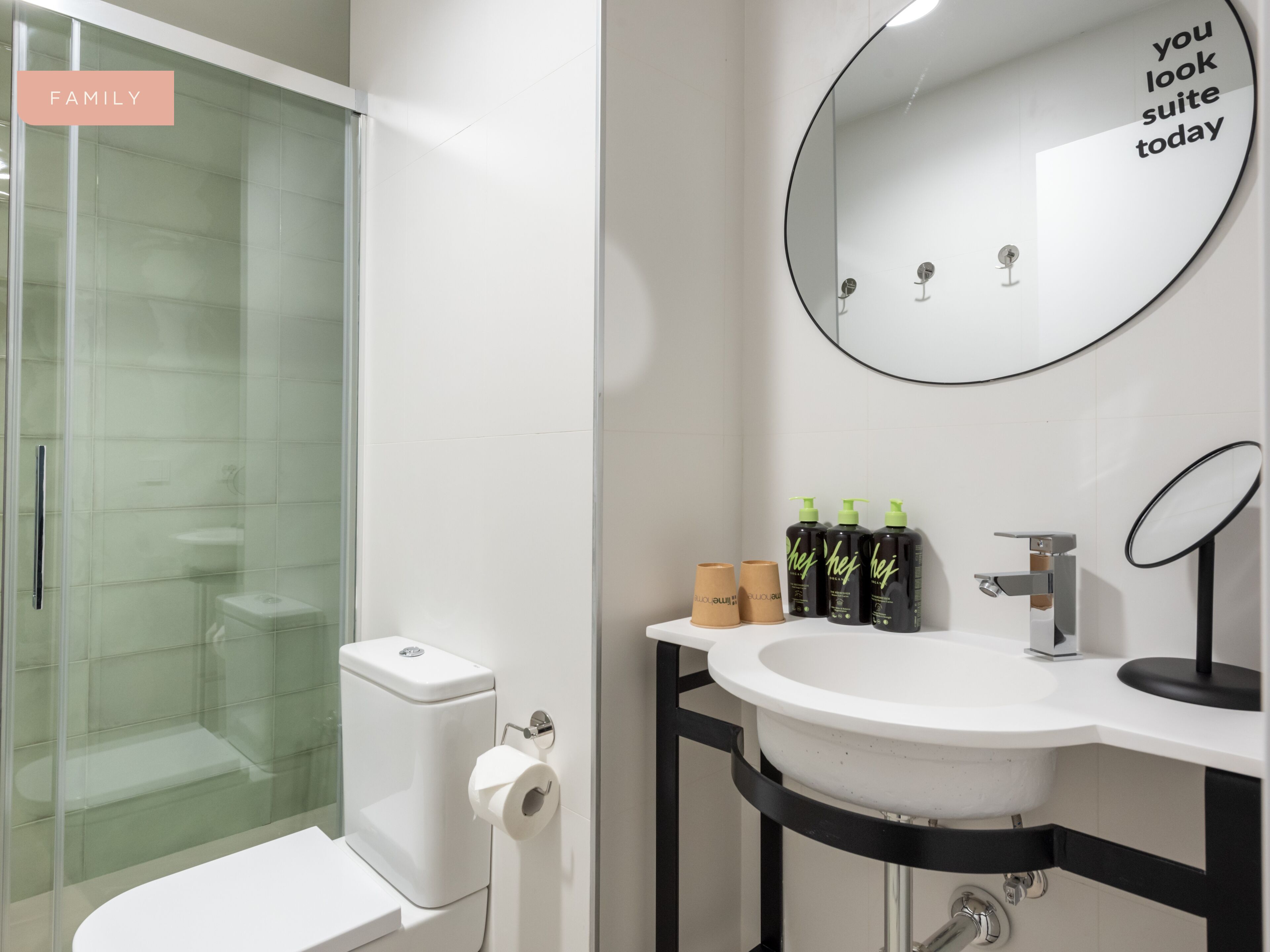 Un baño moderno con cabina de ducha de vidrio, inodoro, lavamanos con espejo y artículos de aseo en la encimera.