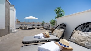 A rooftop lounge with sun loungers, a white umbrella, and a woven hat. - Limehome Sevilla Calle Torcuato Luca de Tena (Seville)