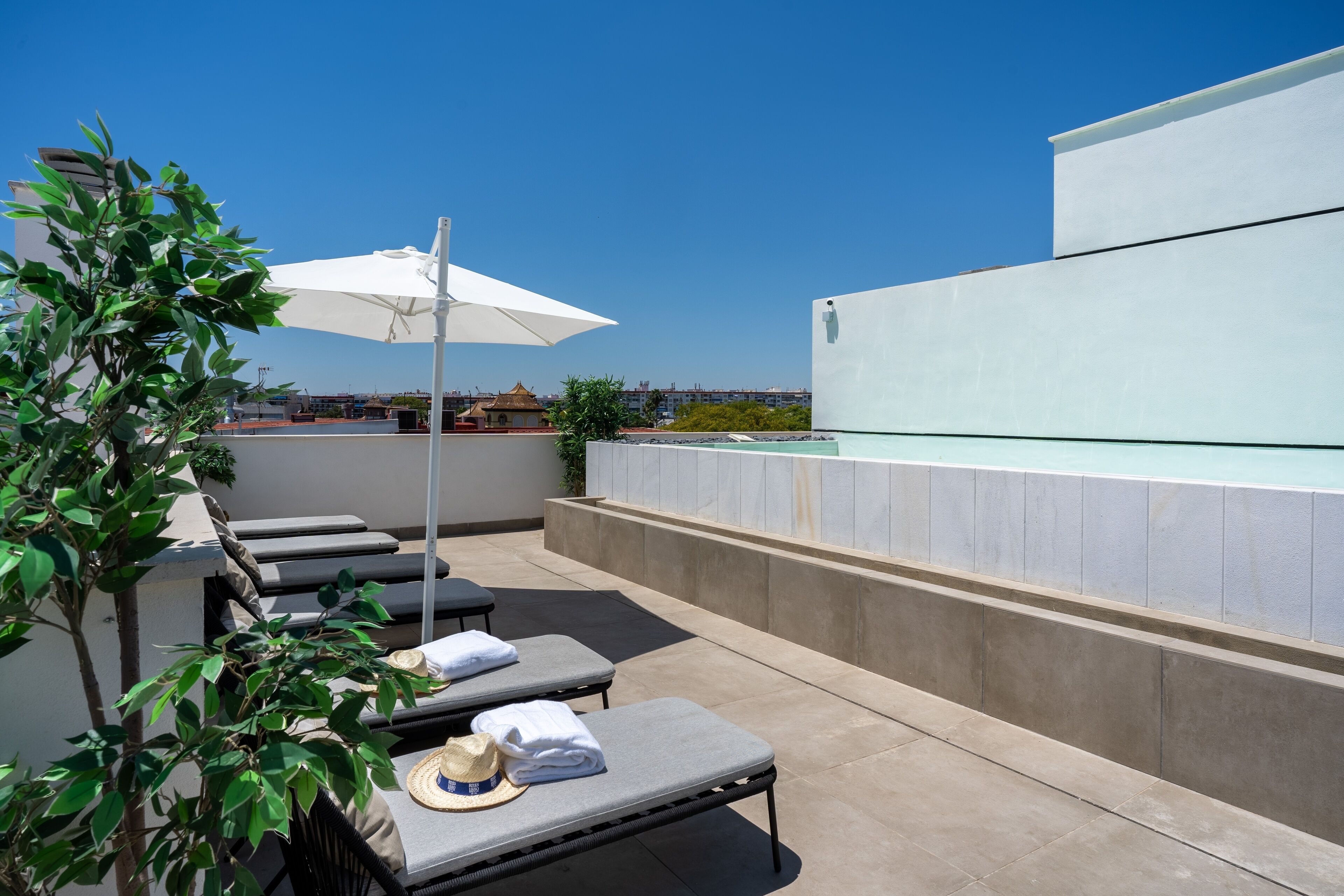 A rooftop lounge with sun loungers, a white umbrella, and a poolside view.
