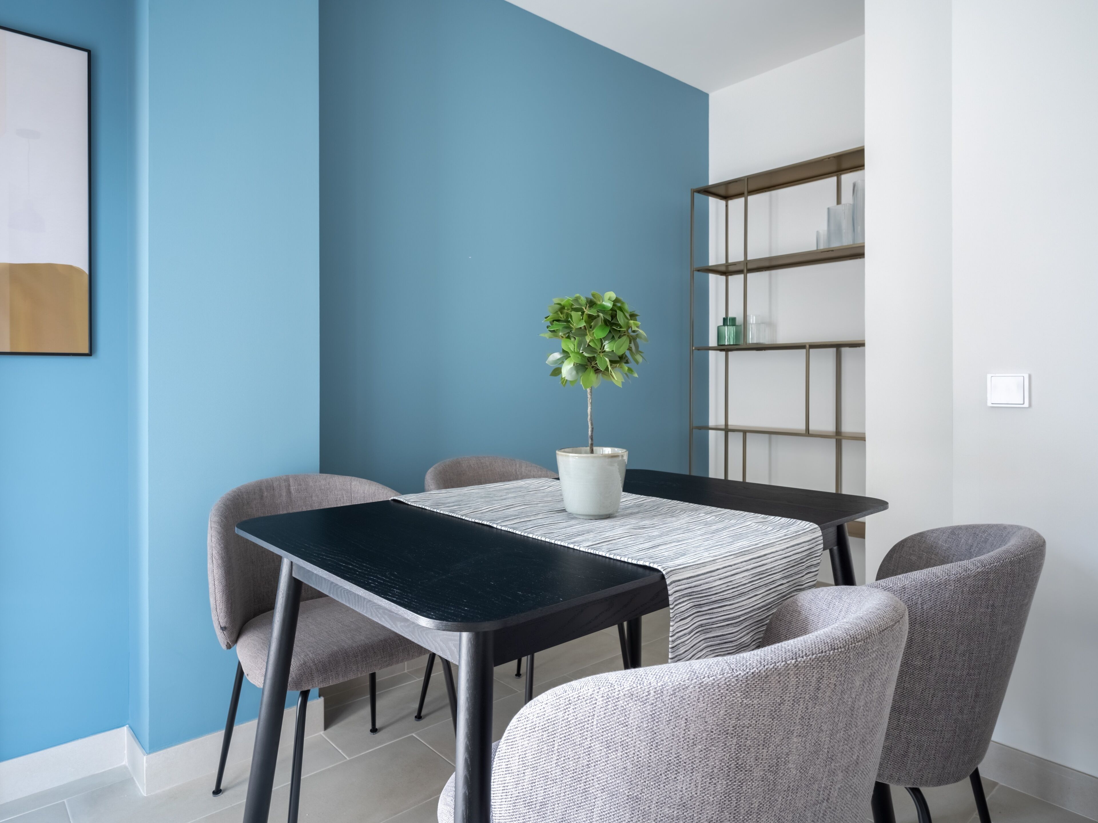 Een moderne eetruimte met een blauwe accentmuur, een potplant en een minimalistische wandplank.