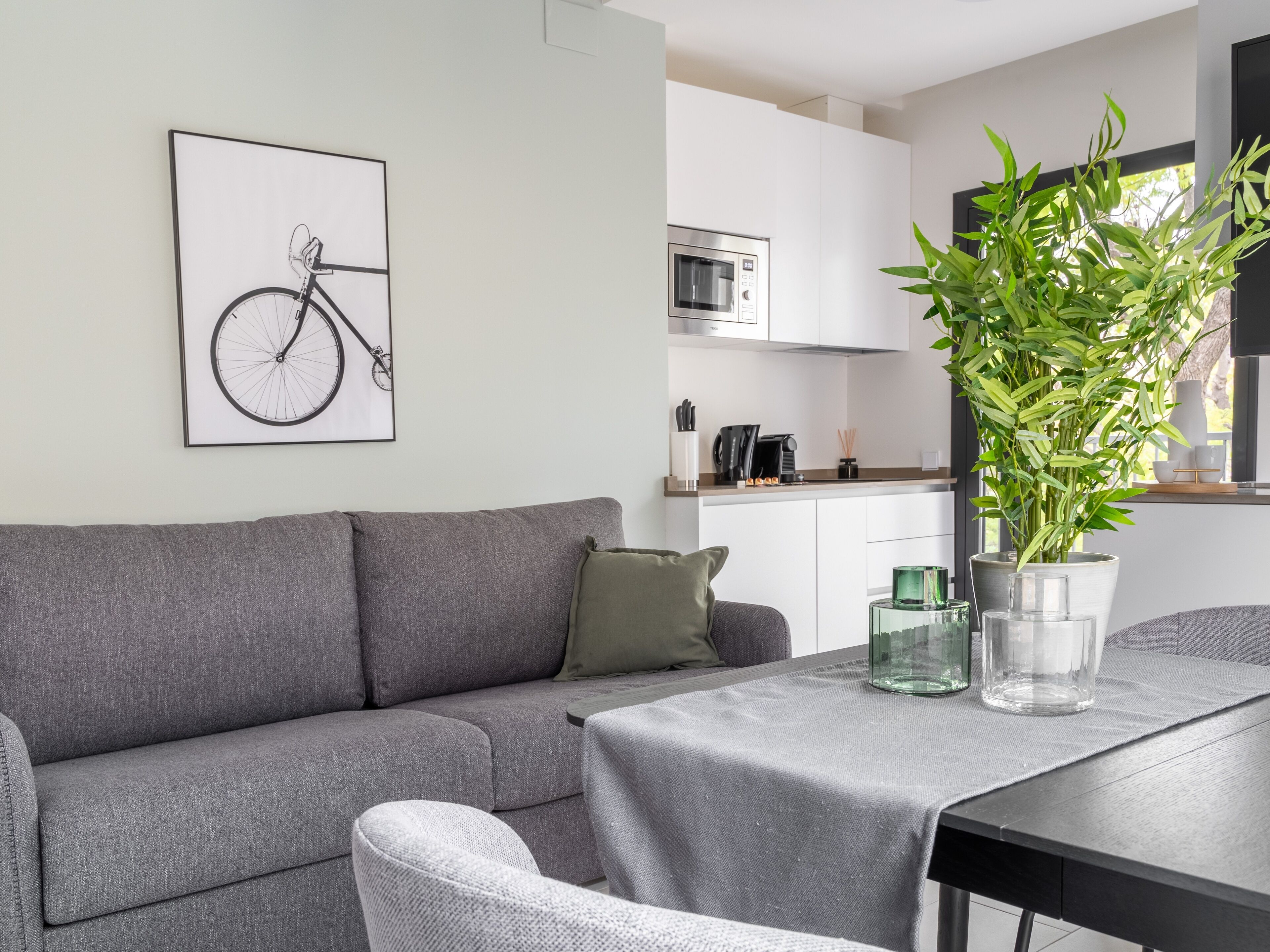 Un salon moderne avec un canapé gris, une table à manger agrémentée d’un vase en verre, et une cuisine en arrière-plan.