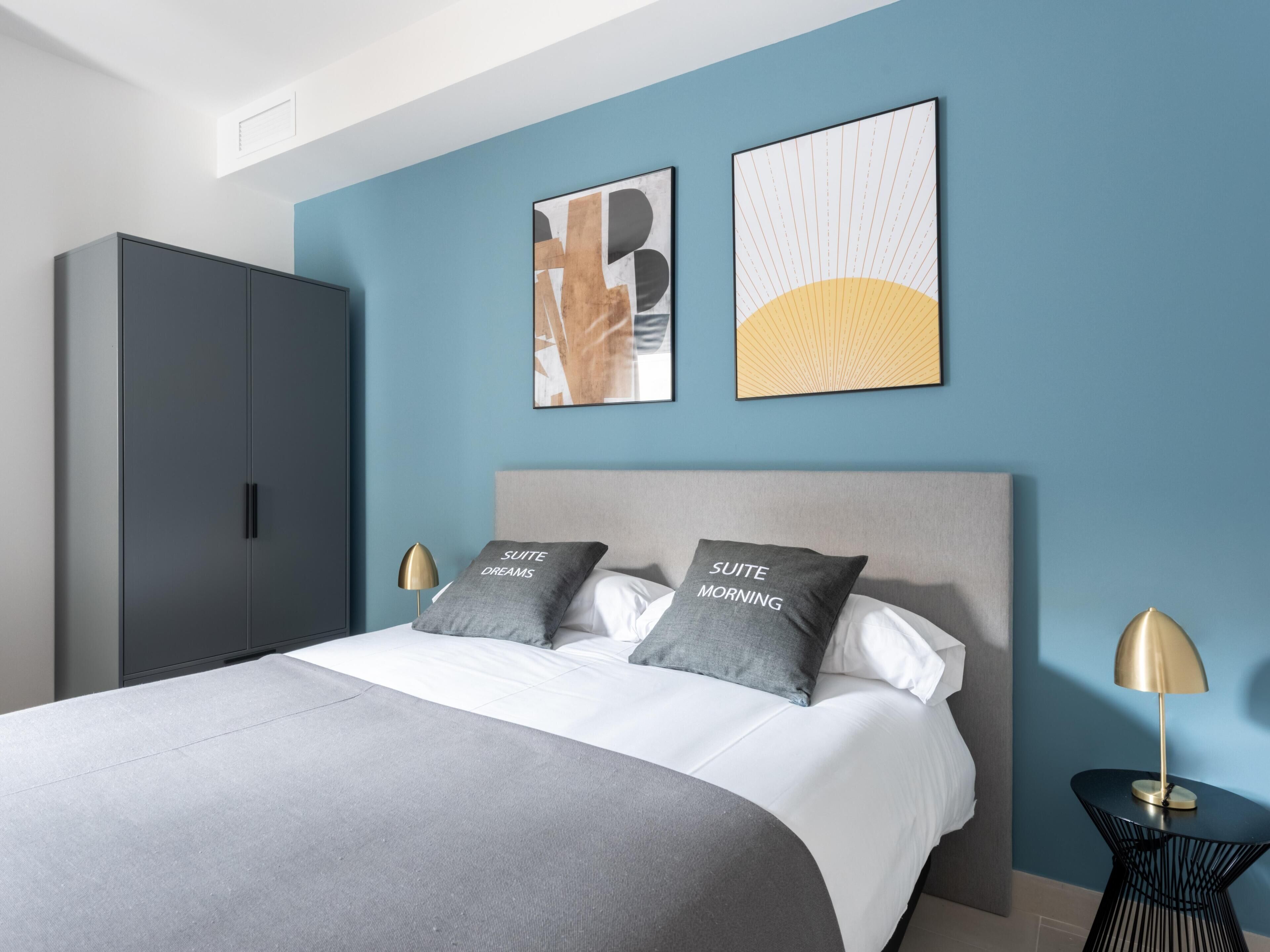 Een moderne slaapkamer met een bed, twee kussens, een nachtkastje, een lamp en een kledingkast.