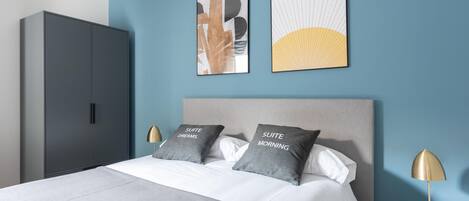 Een moderne slaapkamer met een bed, twee kussens, een nachtkastje, een lamp en een kledingkast.