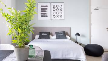 Un dormitorio moderno con una cama, mesitas de noche, una planta en maceta y una obra de arte en la pared.