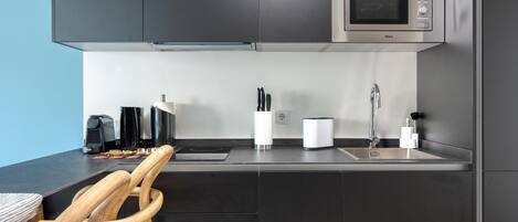 A modern kitchen with dark cabinetry, a built-in microwave, a coffee machine, and a sink with a faucet.