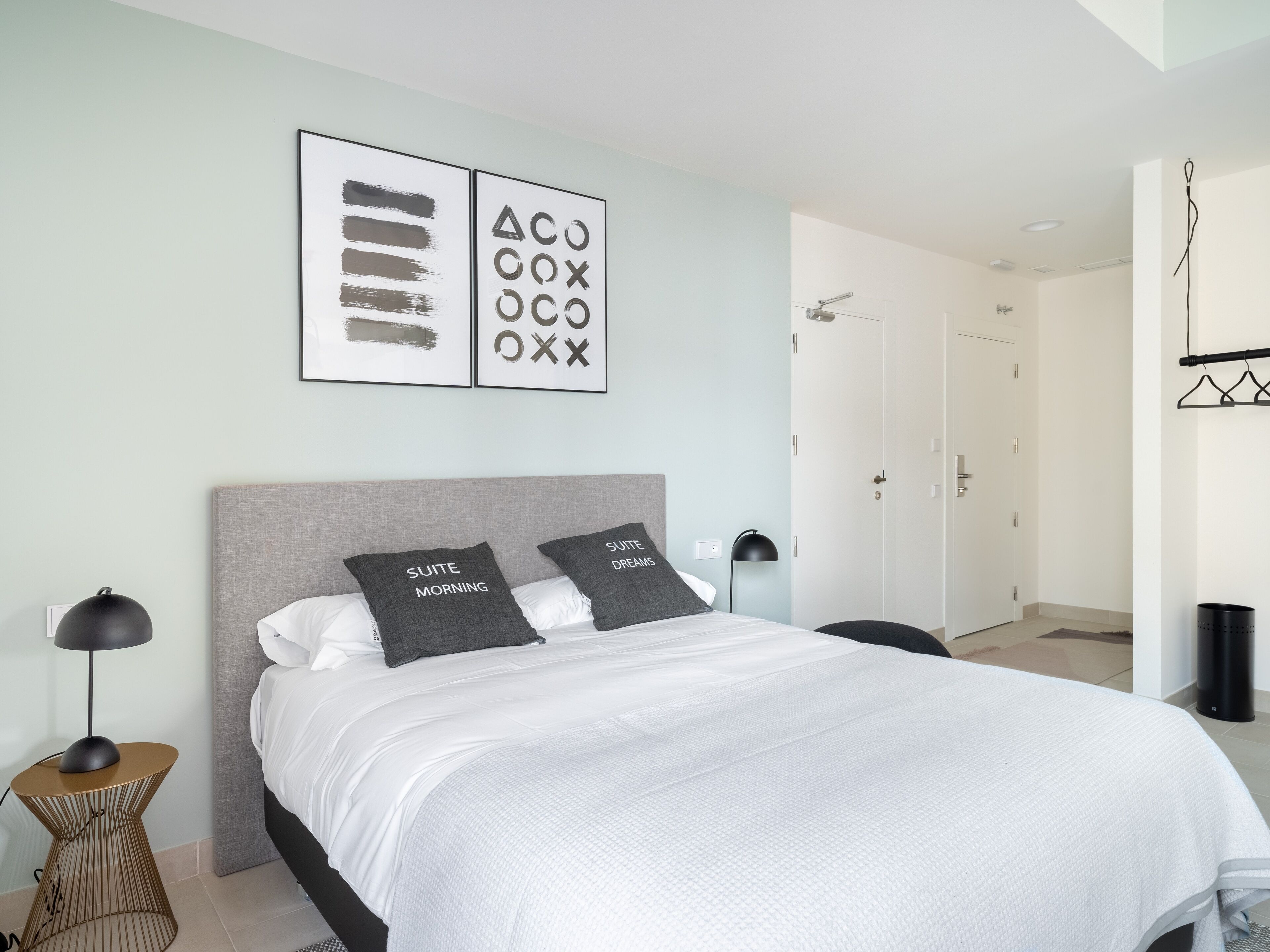 A modern bedroom with a large bed, two bedside tables, a wall-mounted lamp, and a door leading to a bathroom.