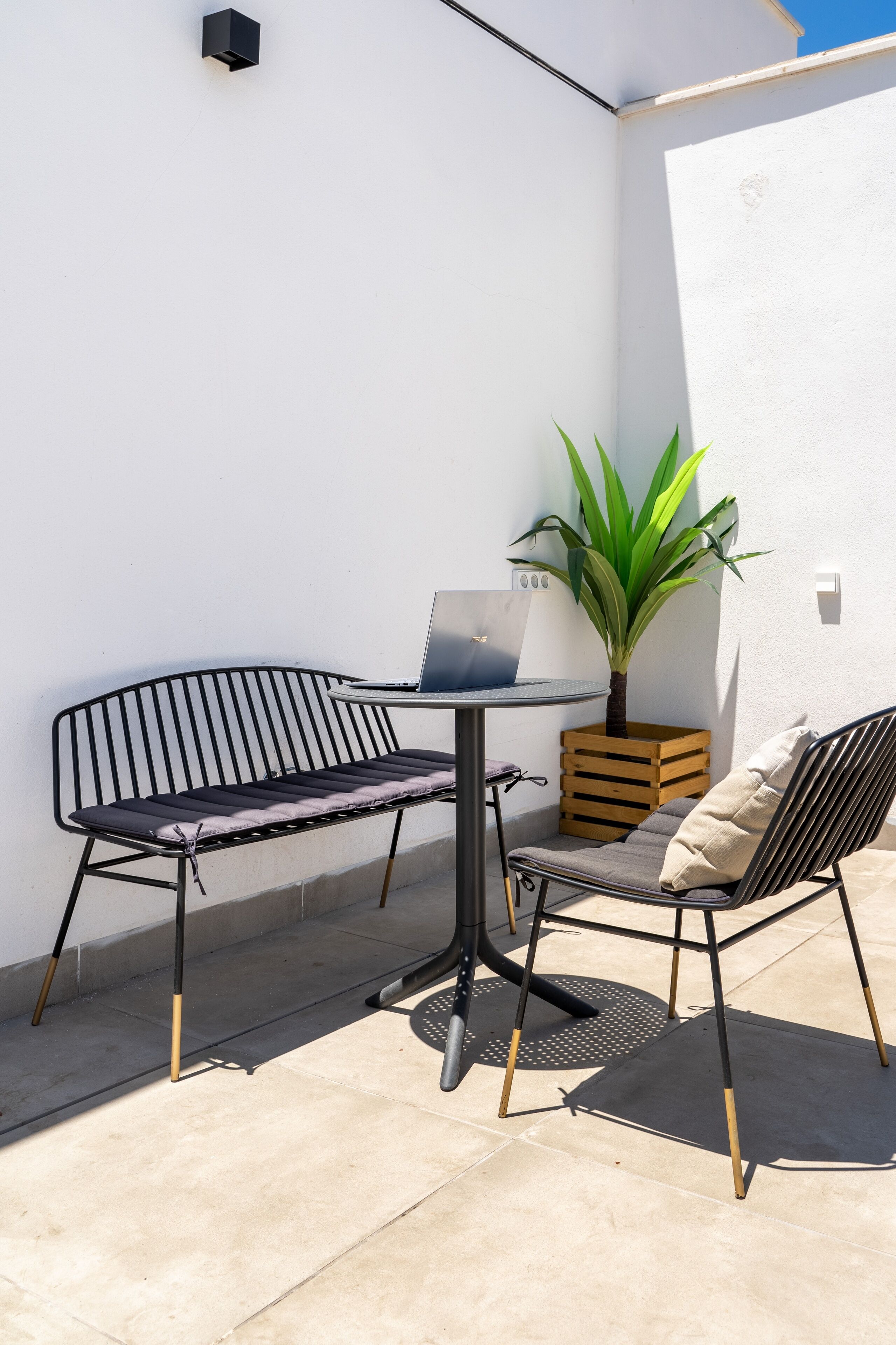 Una pequeña zona de estar al aire libre con una mesa, dos sillas, una computadora portátil y una planta en maceta.