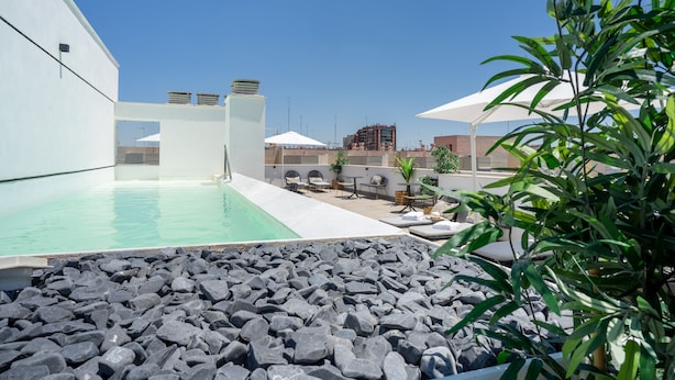 A rooftop pool area with a clear blue sky, a pool surrounded by rocks, and outdoor furniture. - Limehome Sevilla Calle Torcuato Luca de Tena (Seville)