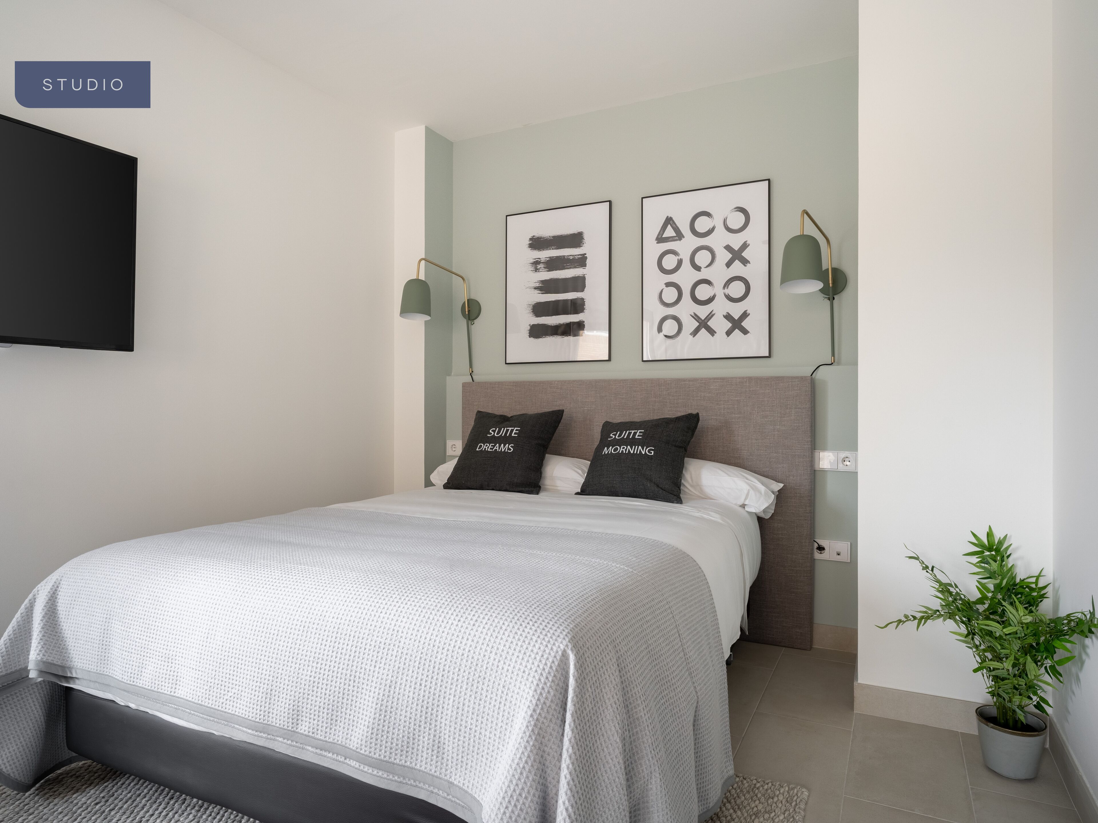 A modern bedroom with a bed, two bedside tables, a wall-mounted TV, and two wall-mounted lamps.