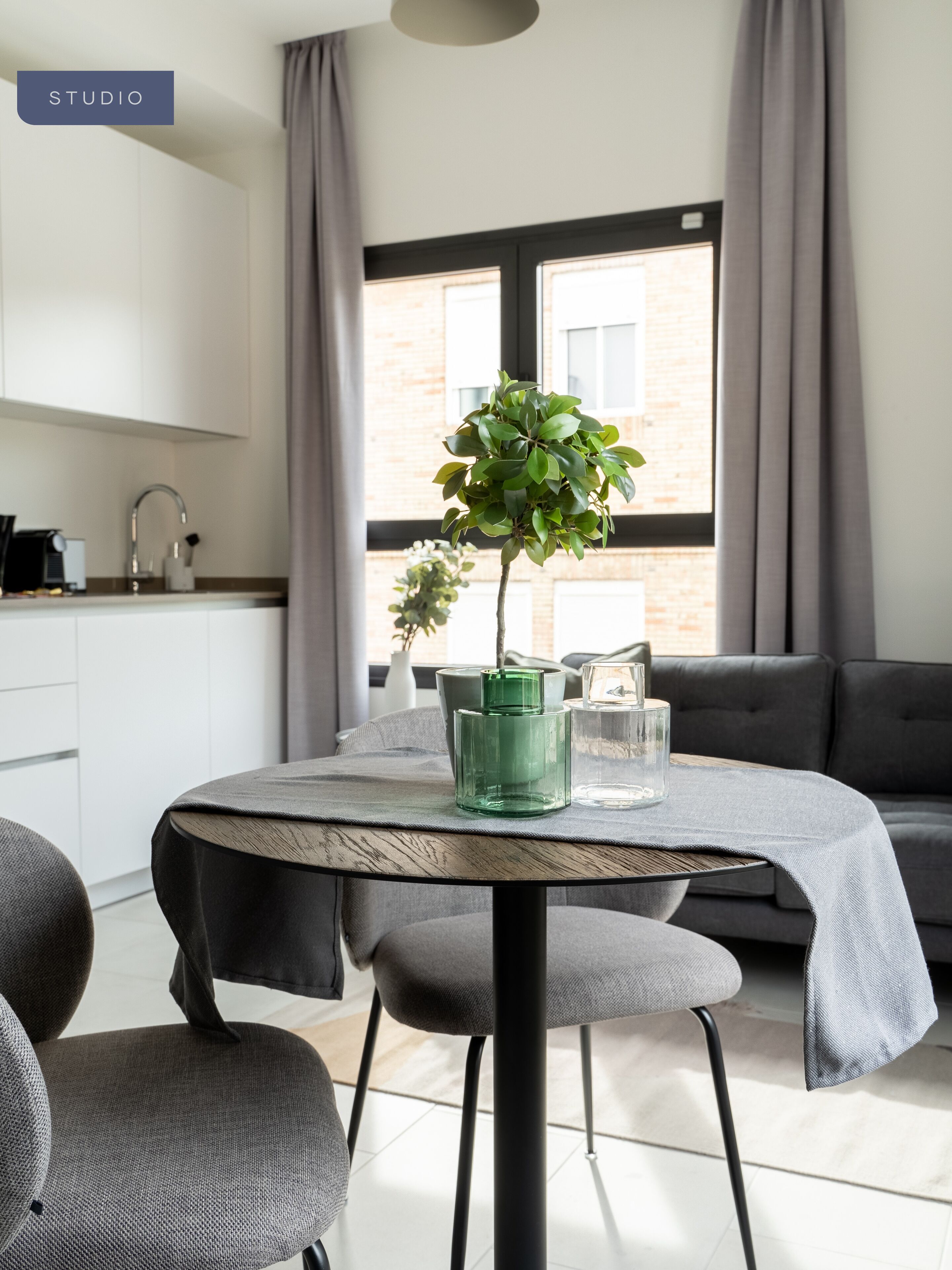 Una cocina moderna con armarios blancos, una mesa redonda con un jarrón verde y un sofá gris.