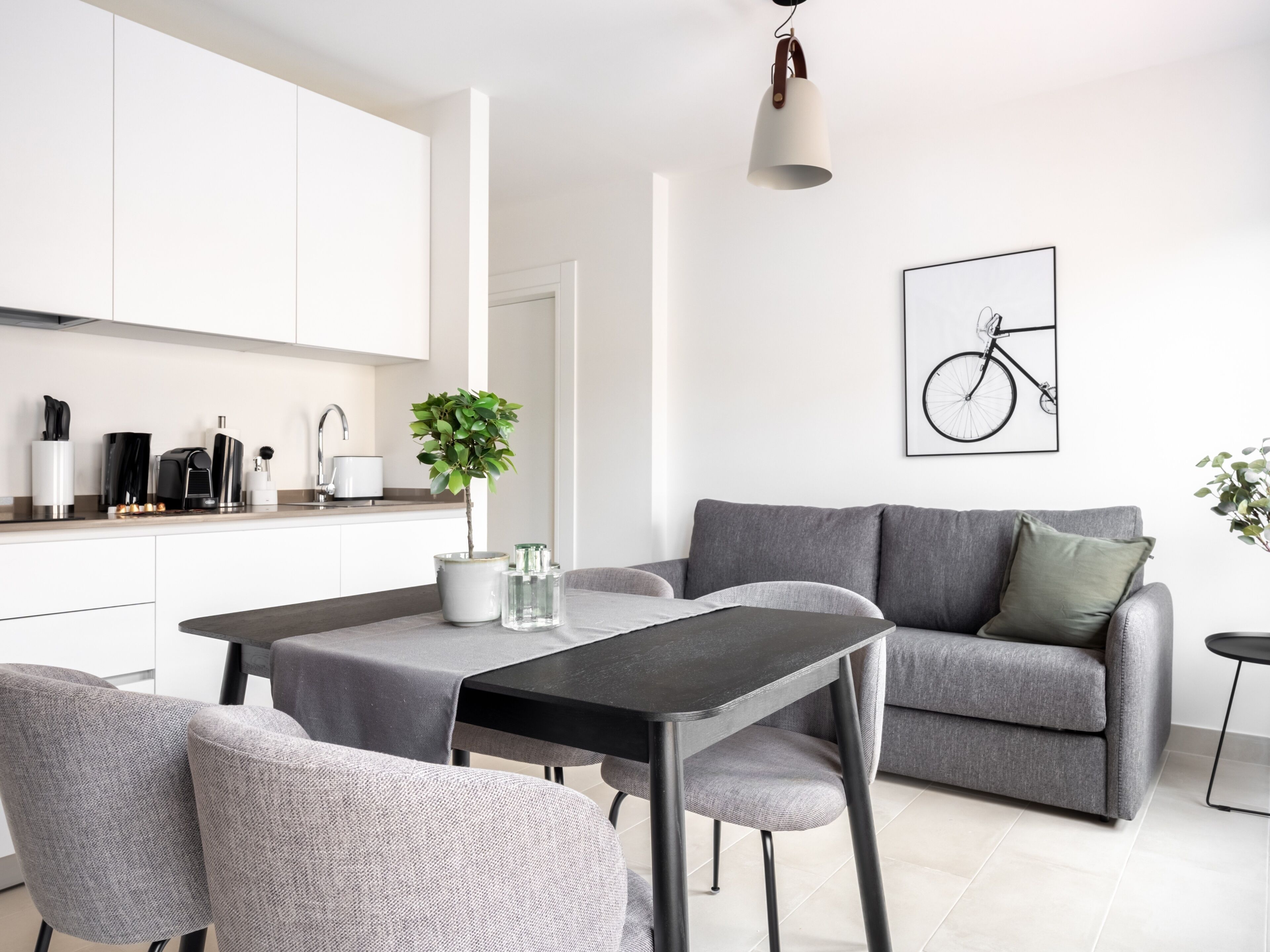 A modern living space with a dining area, grey sofa, and a minimalist kitchen.