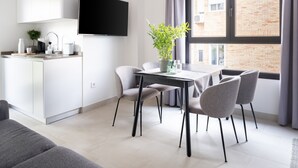A modern kitchen with a flat-screen TV, a dining area with a table and chairs, and a large window with a view of a brick building. - Limehome Sevilla Calle Torcuato Luca de Tena (Seville)