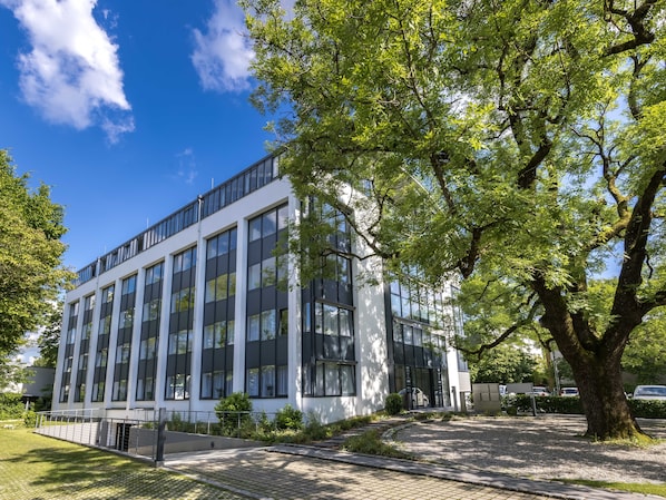 Un edificio moderno con grandes ventanales y un área de entrada pavimentada.
