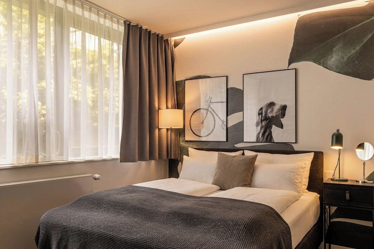 Une chambre d’hôtel moderne avec un grand lit, une table de chevet, une lampe et des œuvres d’art accrochées au mur.