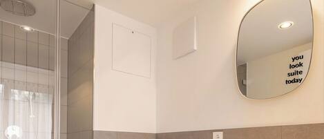 A modern bathroom with a glass shower enclosure, a white toilet, a sink with a mirror, and a wall-mounted light fixture.
