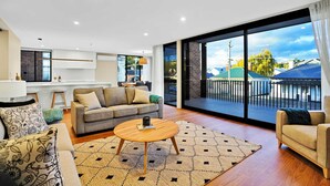 Una sala moderna con sofá, mesa de centro y ventanas amplias que ofrecen vistas a un balcón y edificios vecinos.