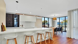 A modern kitchen with white cabinets, a large island with stools, and a dining area with a table and chairs. - Stunning Apartment in the CBD with Parking & WiFi (Launceston)