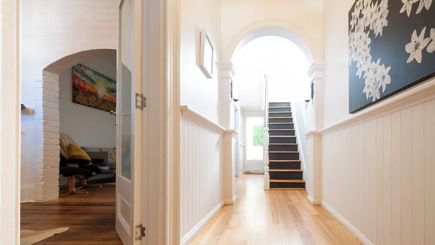 A hallway with wooden flooring, white walls, and a staircase leading to another level.