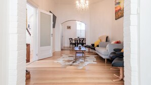 A spacious living area with a wooden floor, a cowhide rug, a grey sofa, and a chandelier.