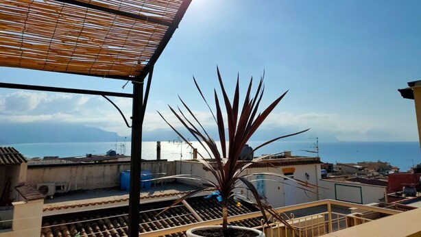 Terraza en la azotea con una planta en maceta, una persiana de bambú y vistas al mar.