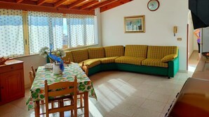 Una habitación acogedora con techo de madera, un sofá verde, una mesa de comedor con sillas y una ventana con cortinas.