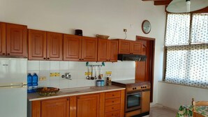 Una cocina con armarios de madera, un refrigerador blanco, una estufa y una ventana con cortinas estampadas.