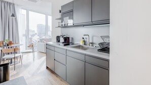 A modern kitchen with grey cabinets, a stainless steel sink, and a window overlooking a cityscape. - Limehome Mönchengladbach Fliethstraße (Moenchengladbach)